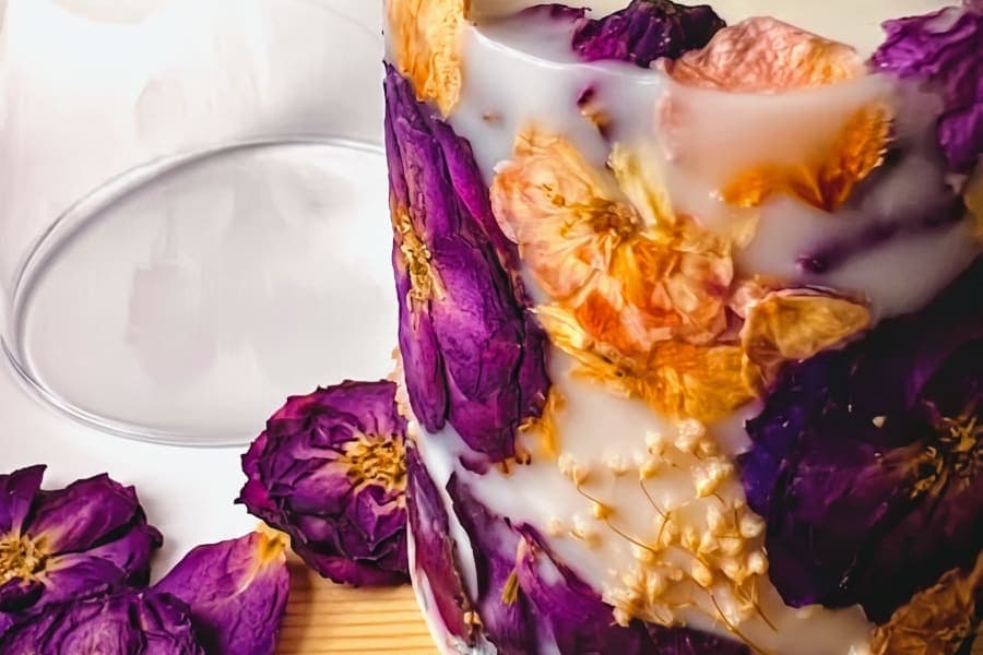 Candera botanical candle with purple and golden pressed flowers set in natural wax.